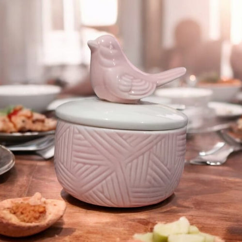 Pink ceramic container with bird lid on a dining table with food.