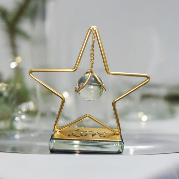 Gold star-shaped decorative item on a white surface with blurred greenery in the background