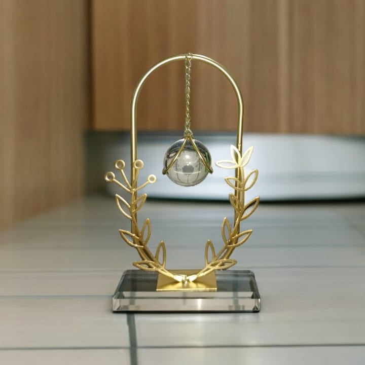 Decorative object with a gold stand and silver sphere on a wooden floor.