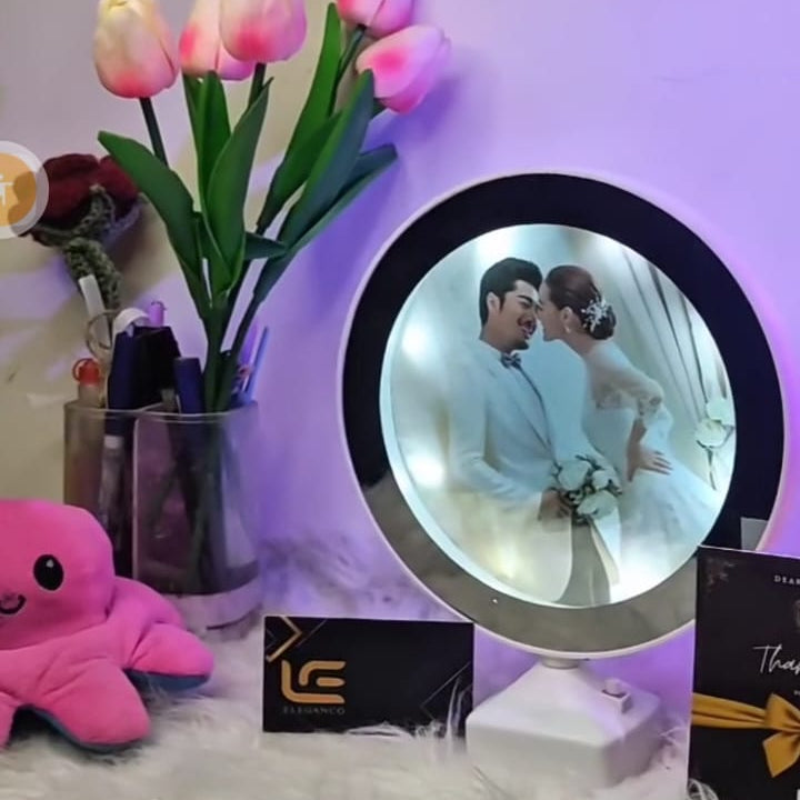 Decorative setup with a circular photo frame, flowers, and plush toys on a textured surface.