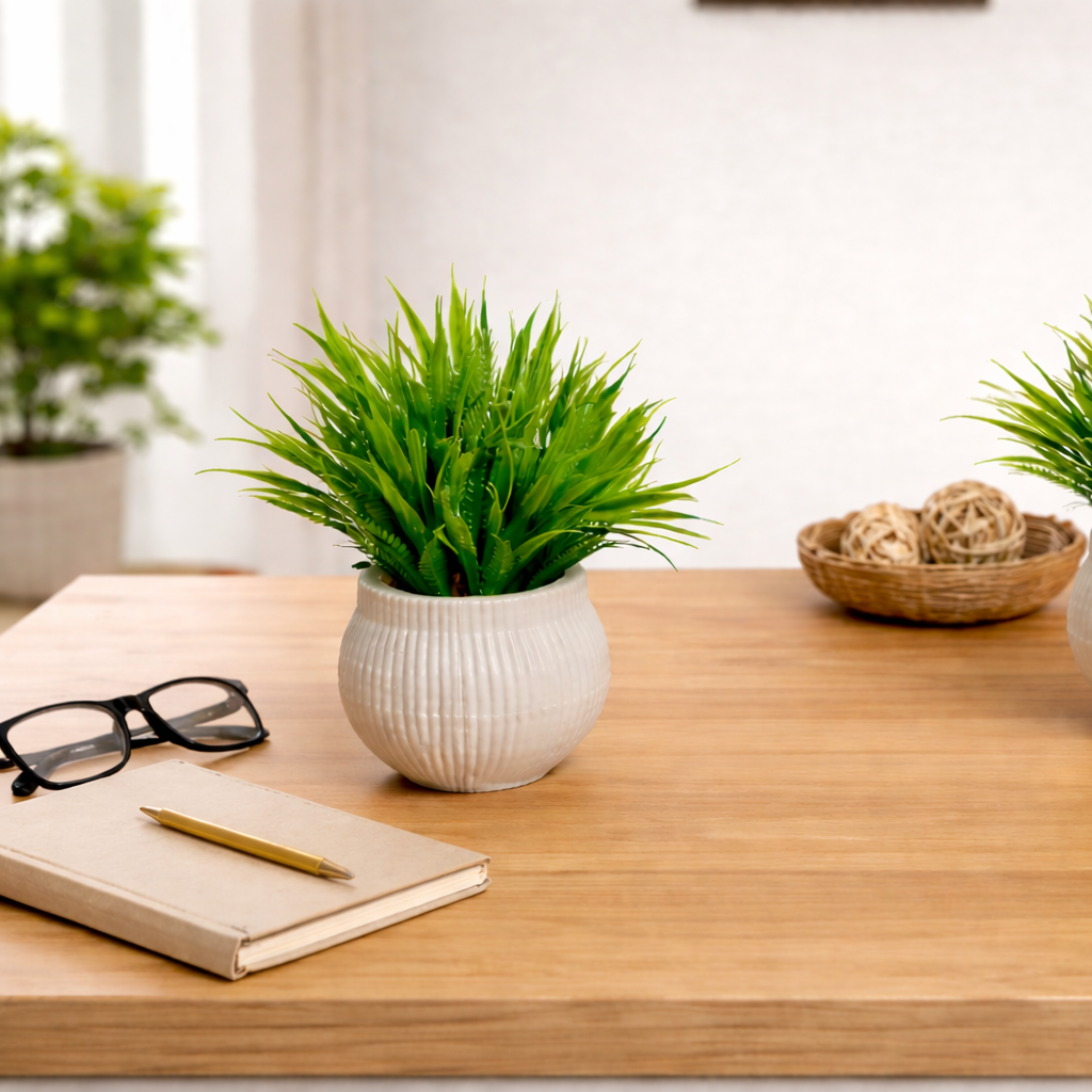 Two potted plants on a wooden desk with a notebook, pen, and coffee cup.
